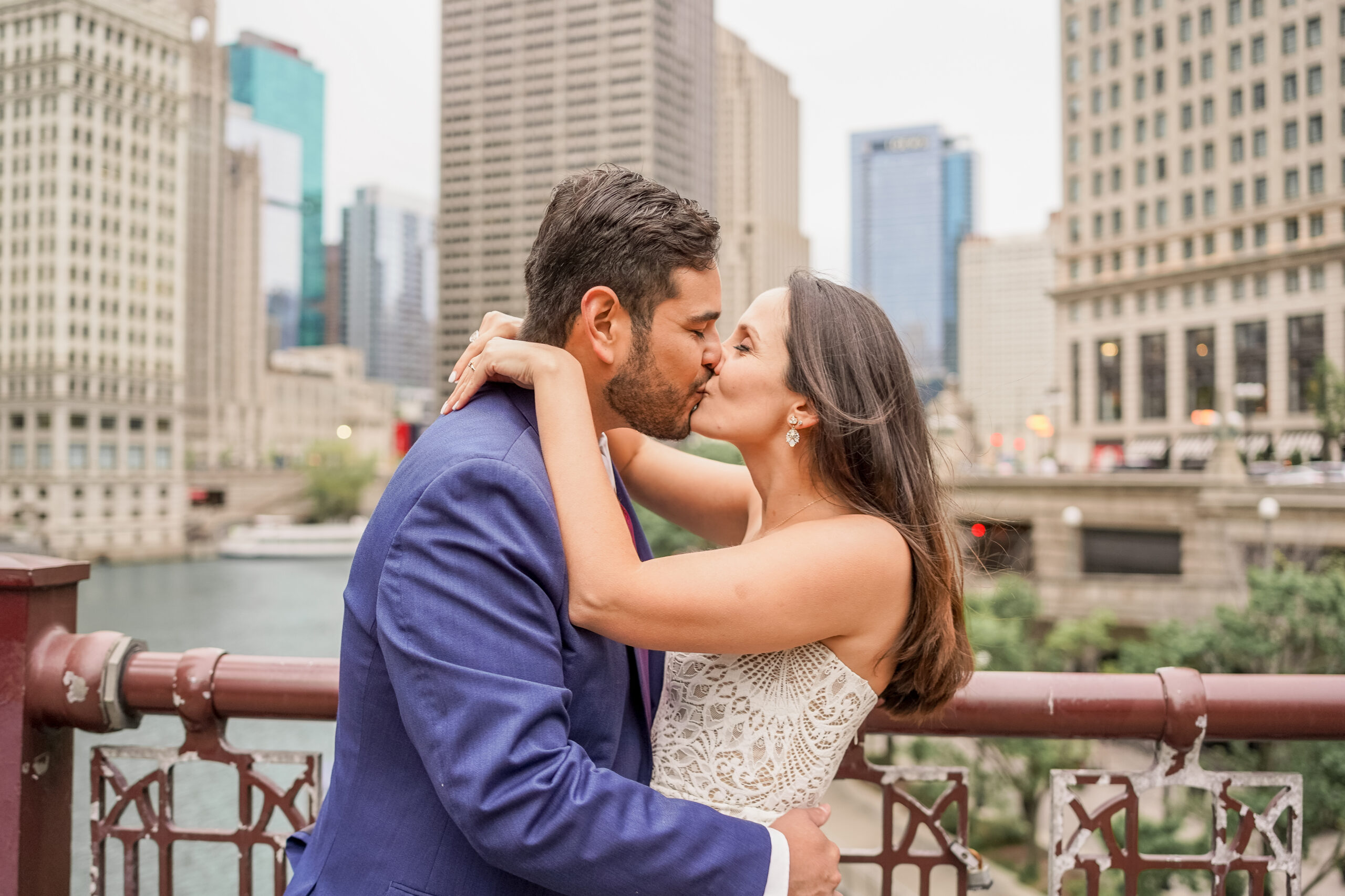 A couple, dressed in fancy clothes, kisses on a bridge over Chicago's riverwalk.