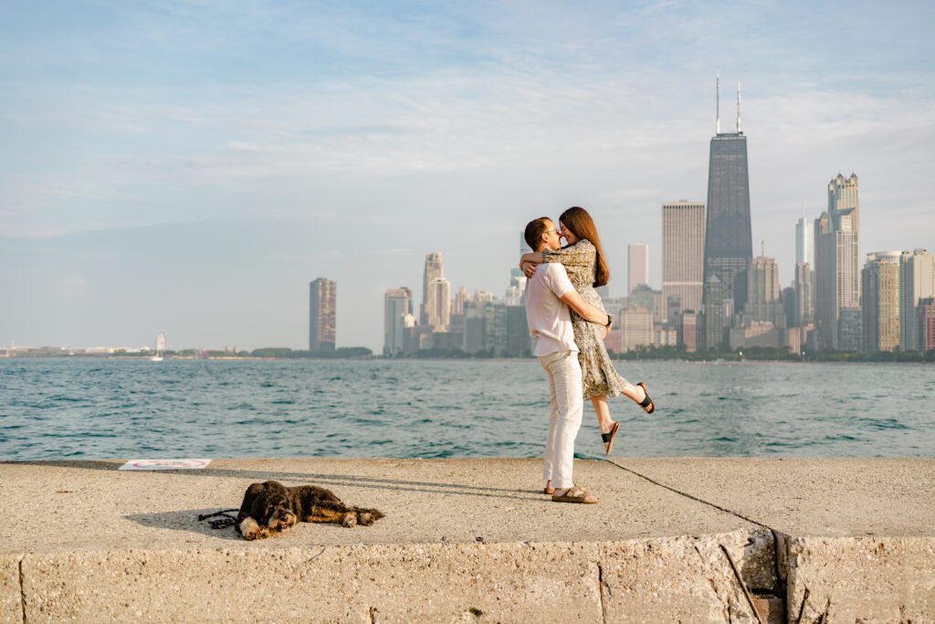 A heterosexual couple embraces on the boardwalk of North Avenue beach while their dog lounges beside them.