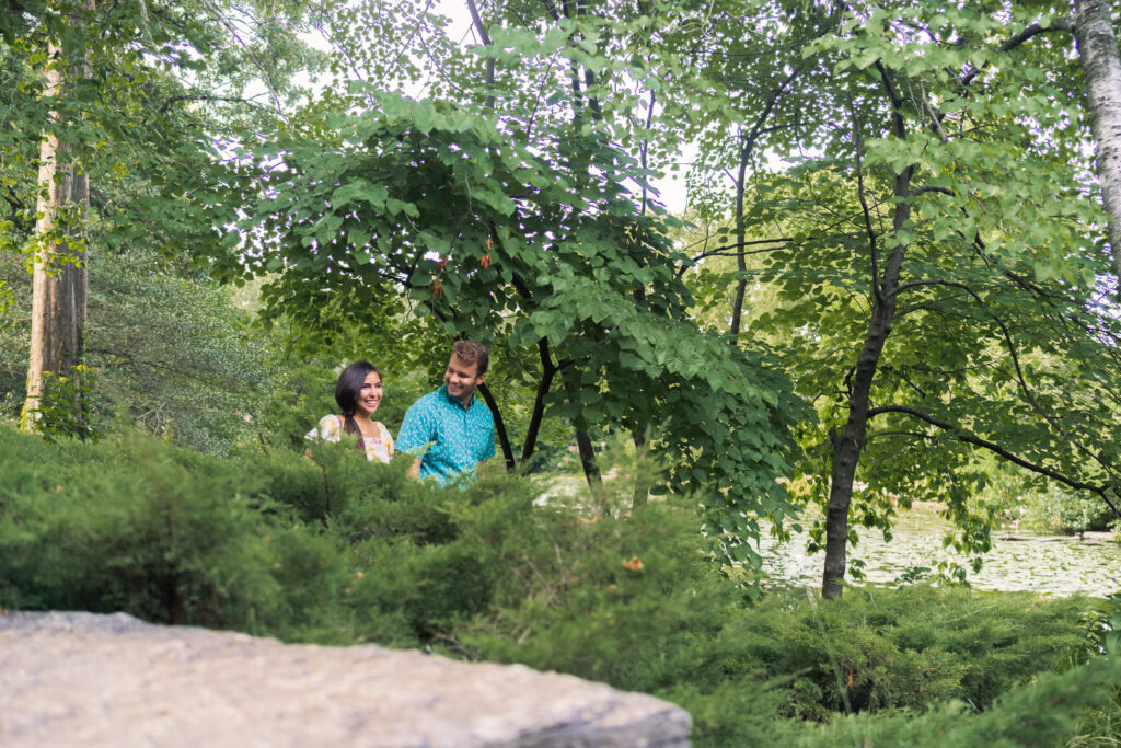 Through lush foliage, a couple is visible walking towards the camera. 
