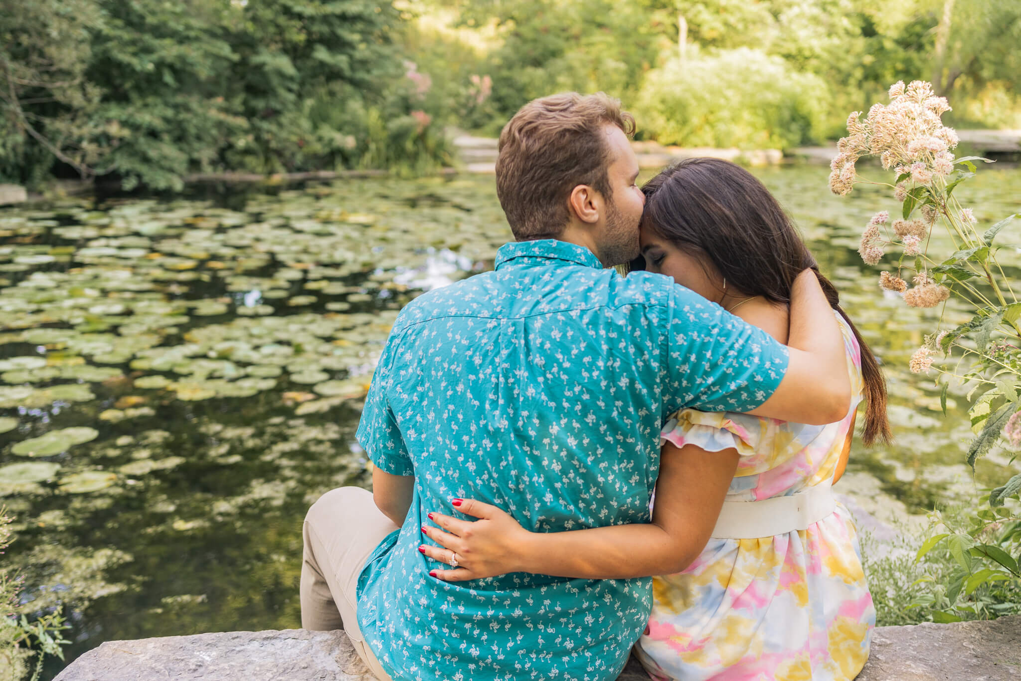A man kisses a woman on the head. We see their backs as they face the expansive magical garden of Chicago's Lily Pool.