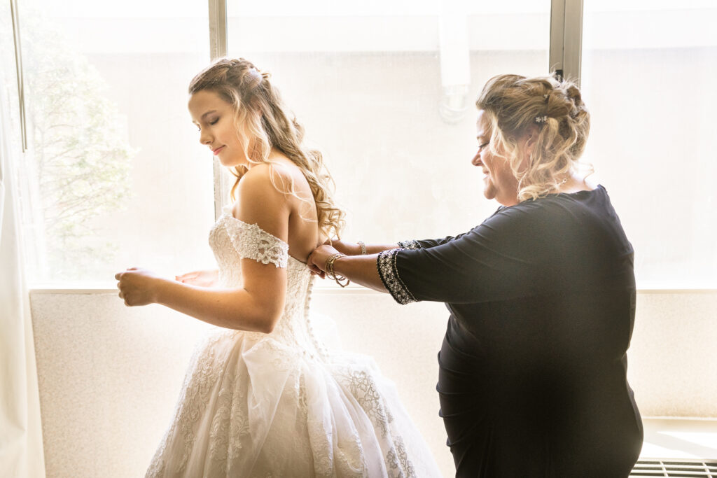mom helping her daughter into her dress at her The Bridgeport Art Center wedding