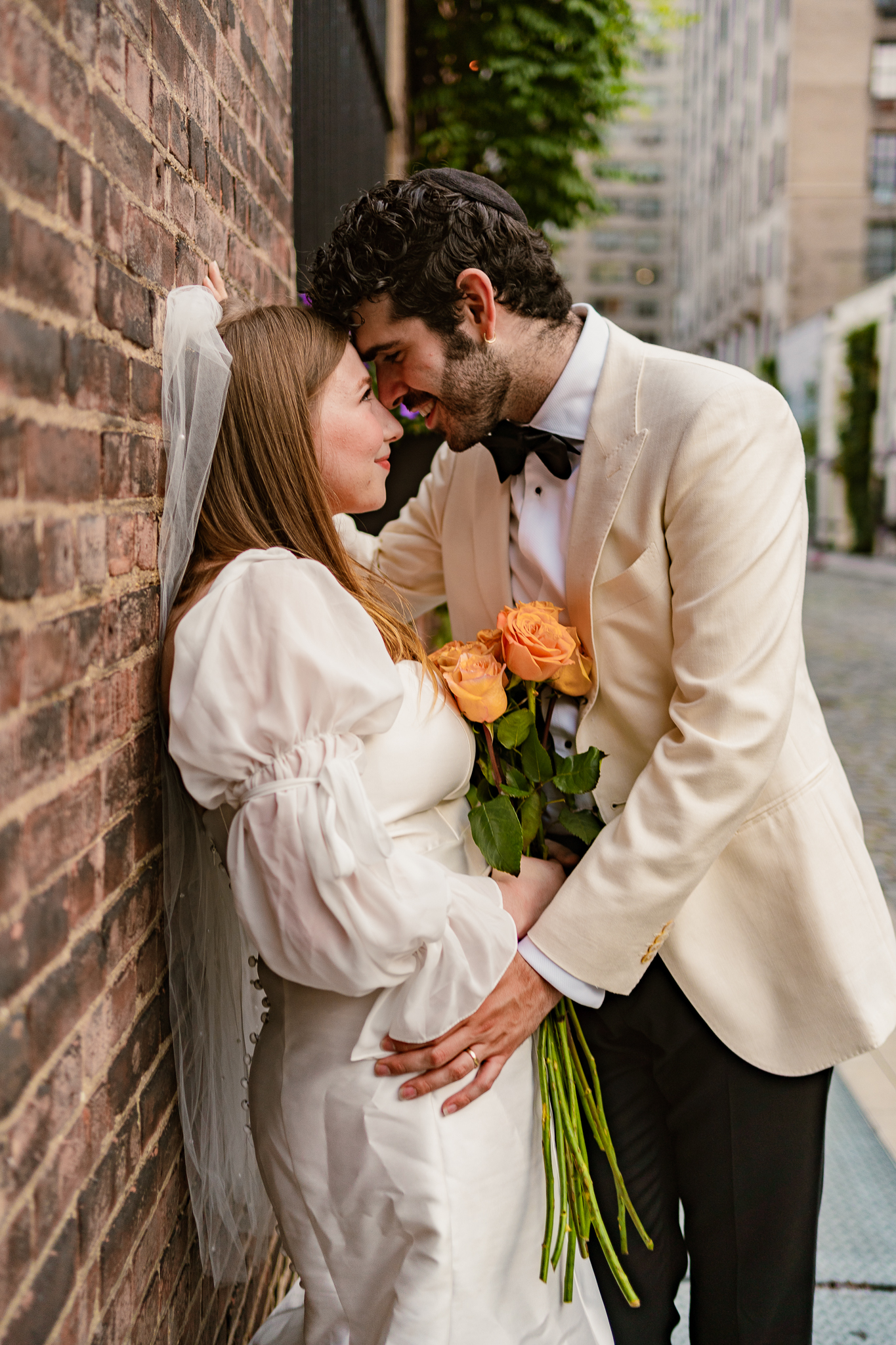groom and bride leaning against a brick wall while being photographed by a Jewish Wedding Photographer