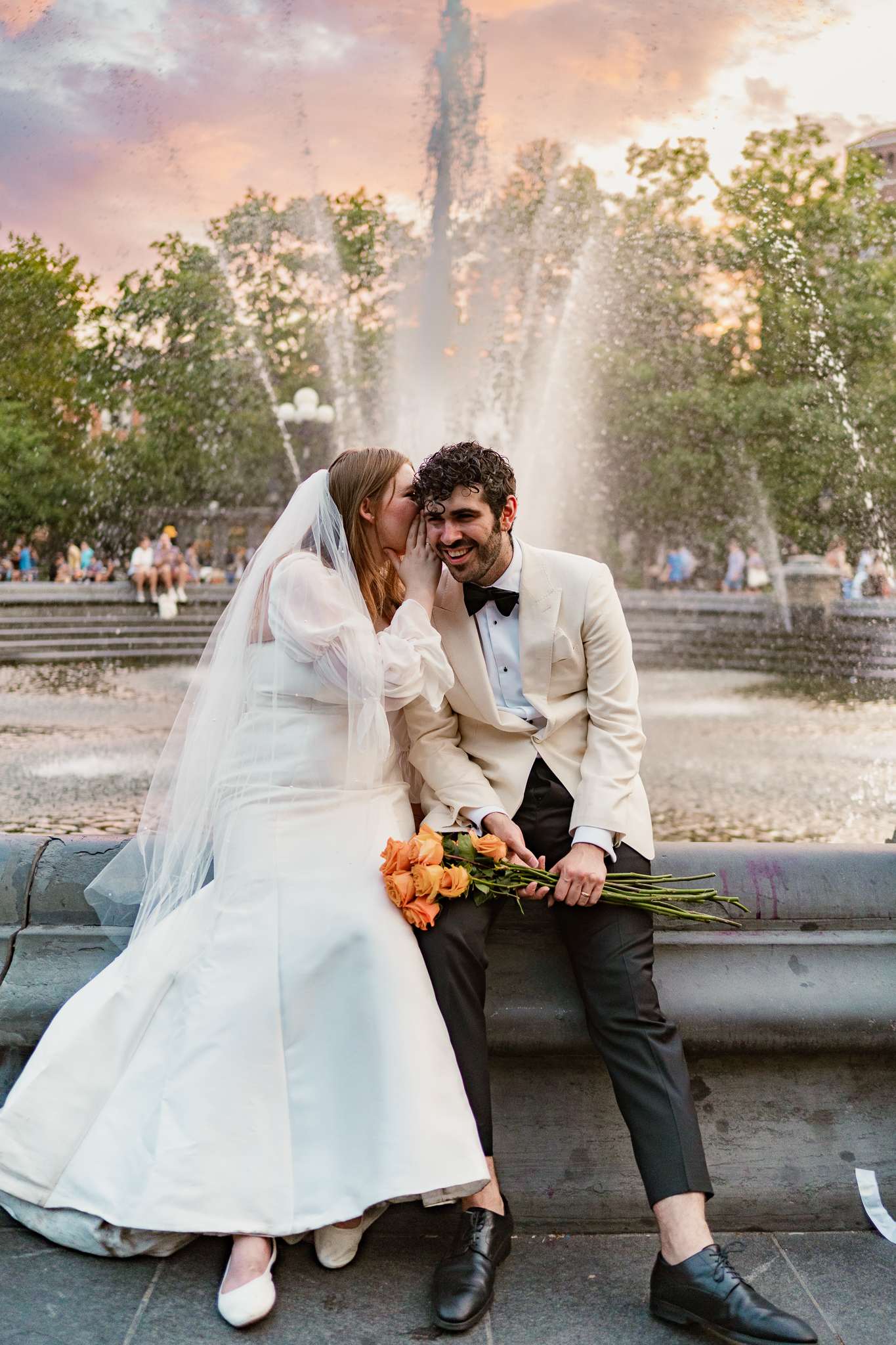 bride kissing her groom on the cheek in front of a fountain