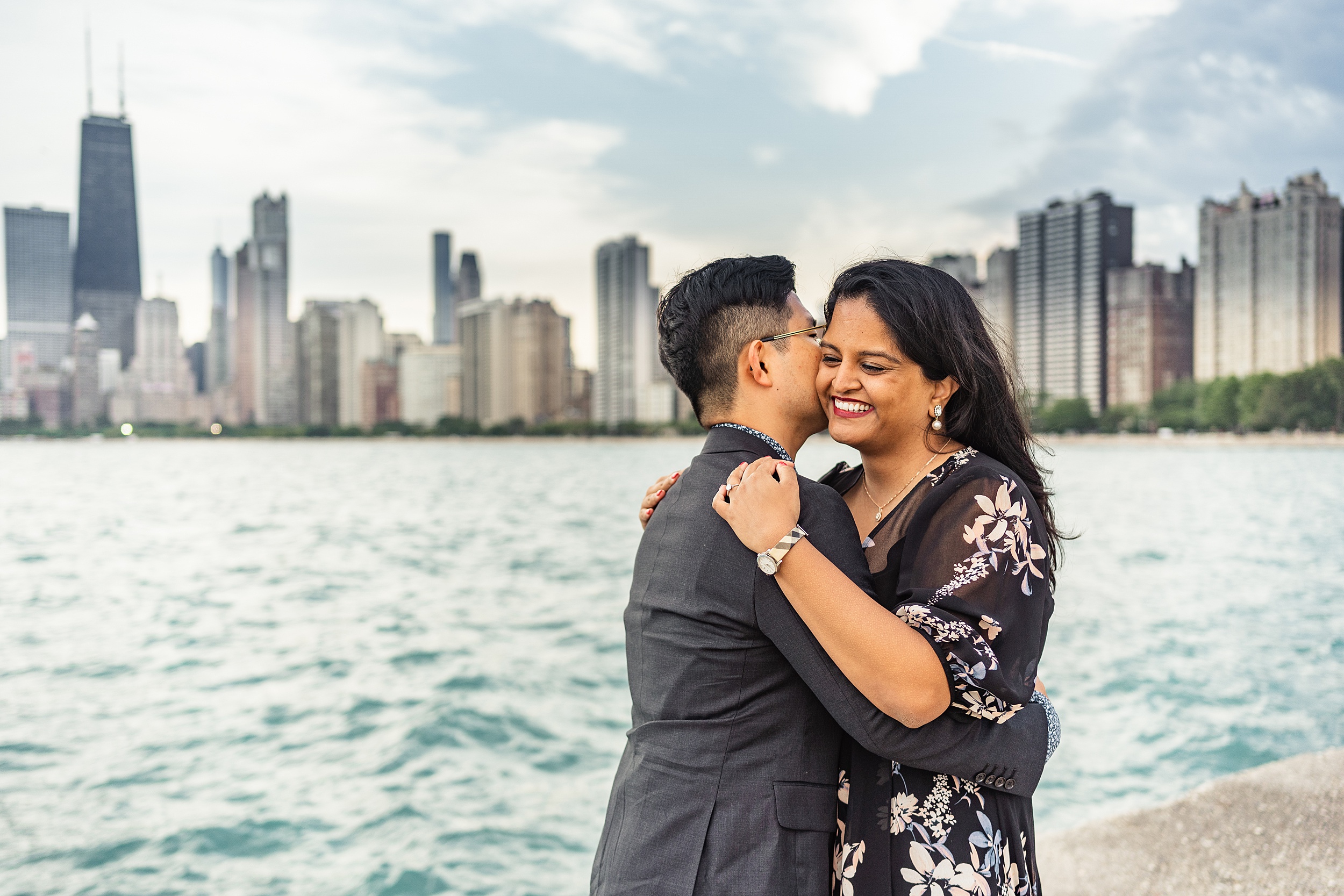 man kissing woman on the cheek near the water with the chicago skyline behind them chicago engagement photos