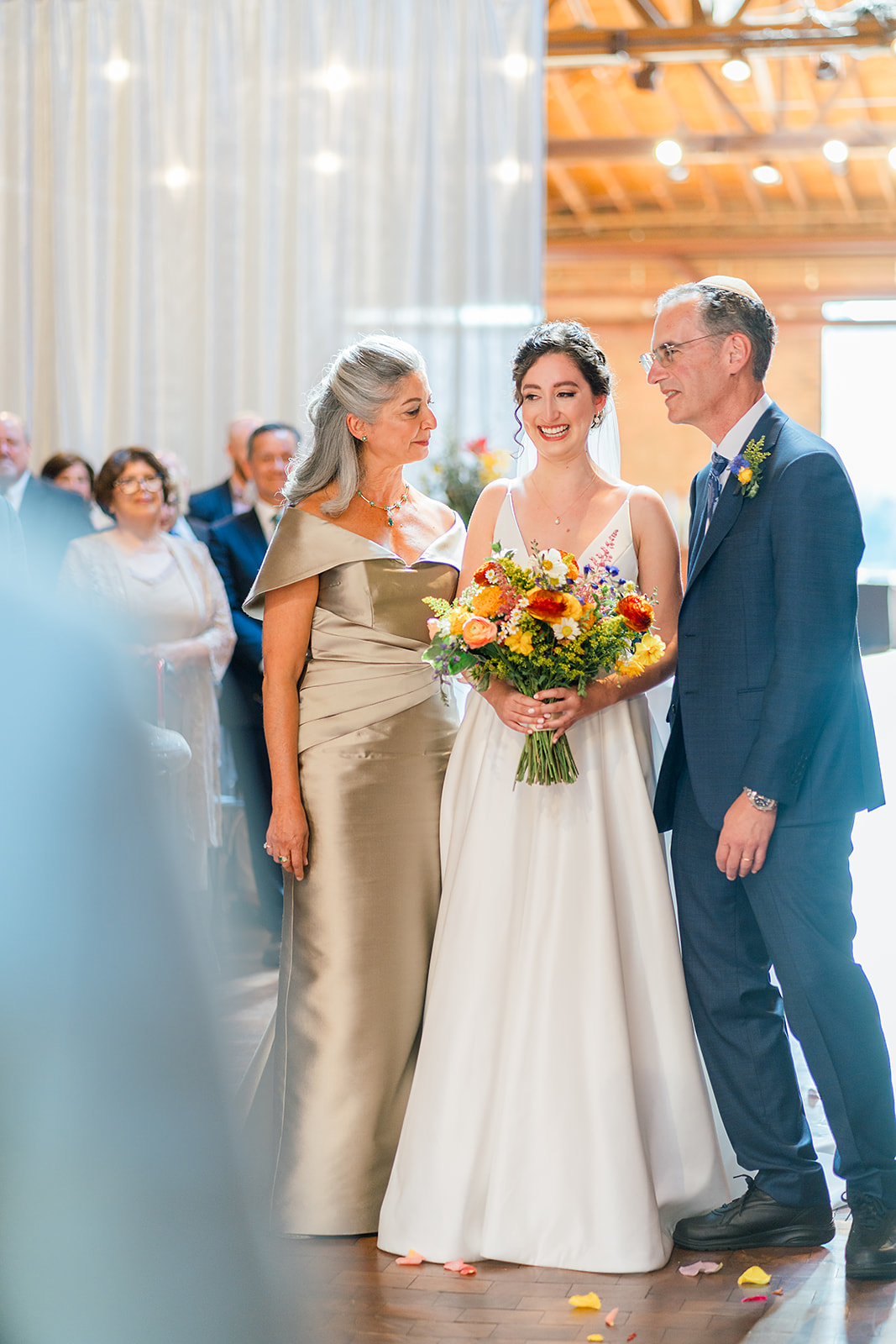 A bride smiles big while mom and dad walk her down the aisle