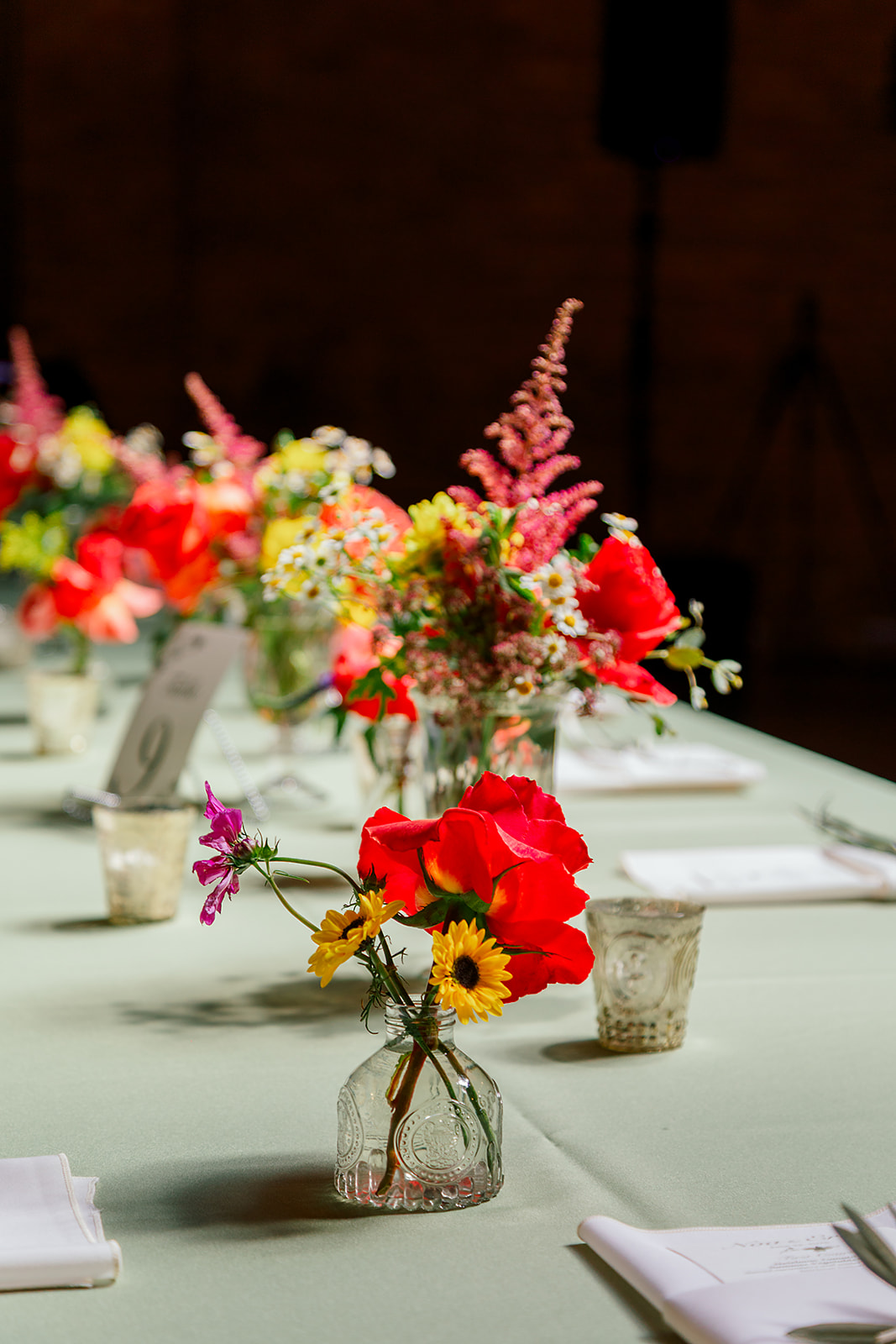 Details of a vibrant floral centerpiece among many on a long reception table with green linen