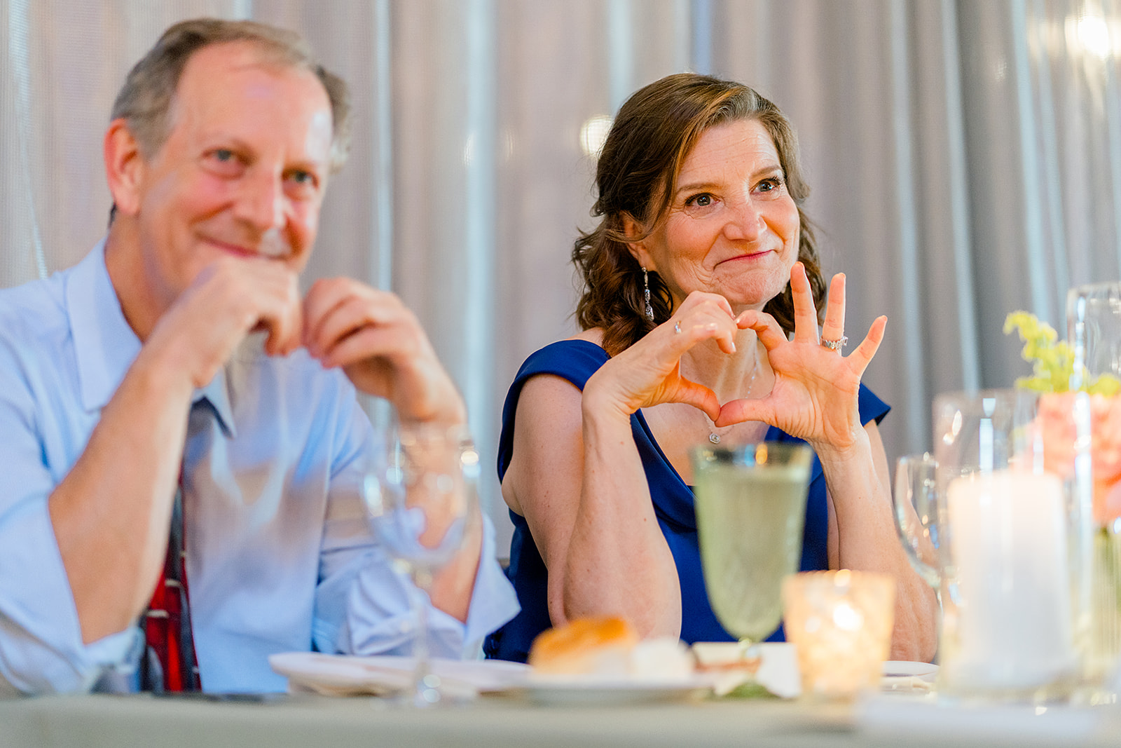 A mother makes a heart shape at a reception table to her child during their wedding