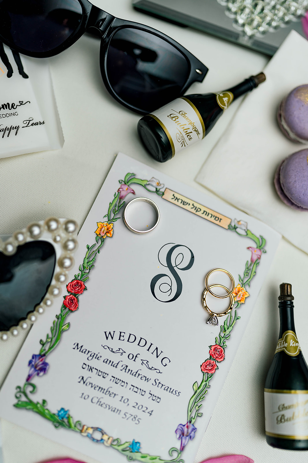 Bridal details laying on a white table with tiny bubble bottles, rings and invitations