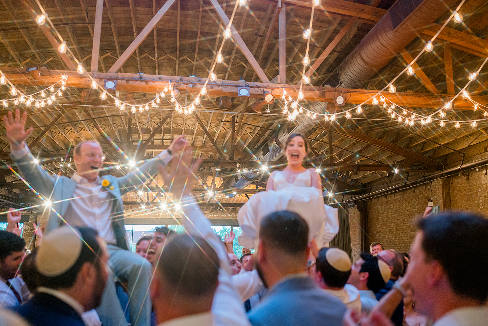 Newlyweds are lifted under the market lights while sitting in chairs during their reception
